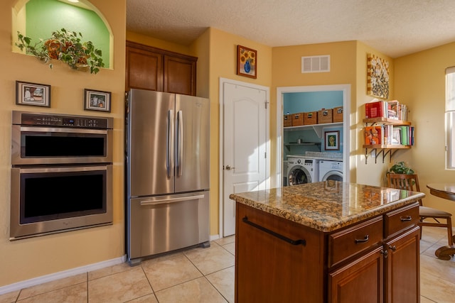 kitchen featuring a textured ceiling, a center island, stainless steel appliances, dark stone countertops, and independent washer and dryer