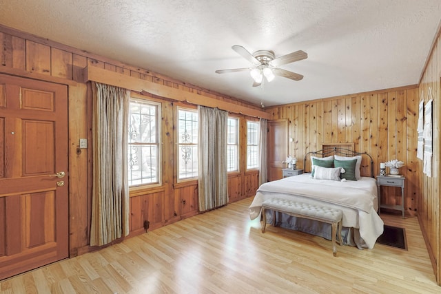 bedroom featuring ceiling fan, a textured ceiling, wood walls, and light wood-type flooring