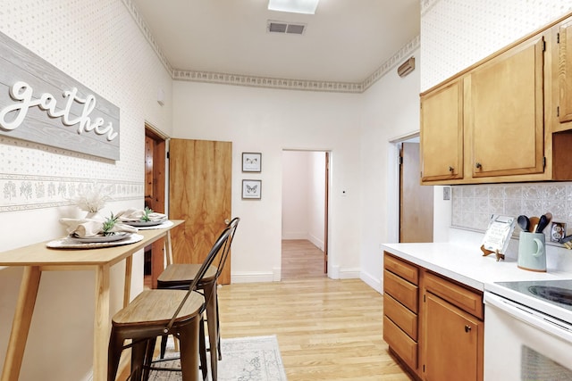 kitchen featuring tasteful backsplash, white range with electric cooktop, and light wood-type flooring