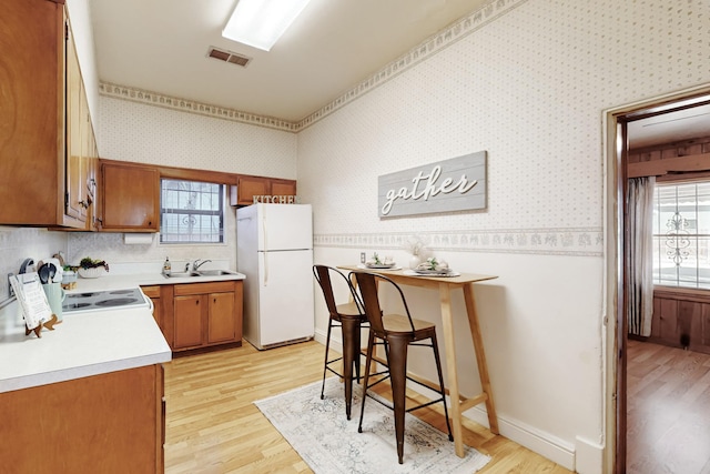 kitchen featuring a kitchen bar, sink, white appliances, and light hardwood / wood-style flooring