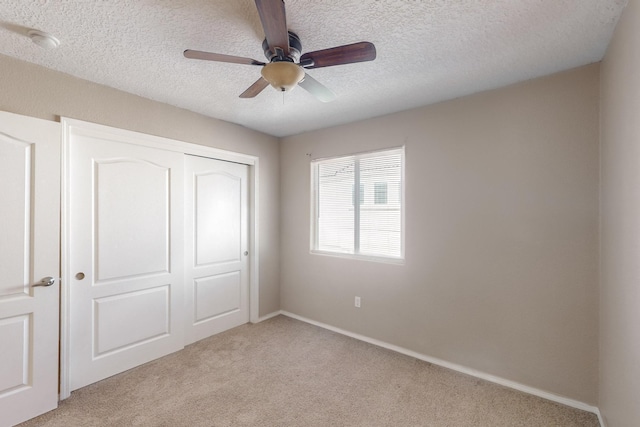 unfurnished bedroom featuring ceiling fan, a closet, light carpet, and a textured ceiling