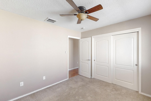 unfurnished bedroom featuring ceiling fan, a textured ceiling, a closet, and light carpet