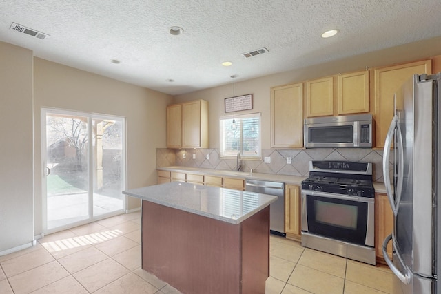 kitchen with appliances with stainless steel finishes, a kitchen island, decorative backsplash, hanging light fixtures, and light tile patterned floors