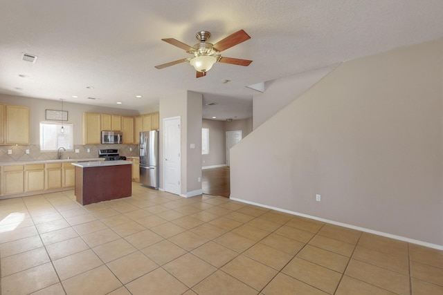 kitchen with light brown cabinetry, light tile patterned flooring, stainless steel appliances, and a kitchen island