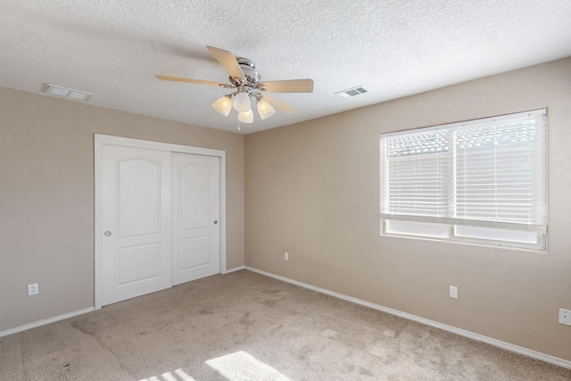 unfurnished bedroom with ceiling fan, light colored carpet, a closet, and a textured ceiling