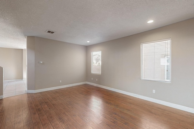 spare room featuring plenty of natural light, wood-type flooring, and a textured ceiling