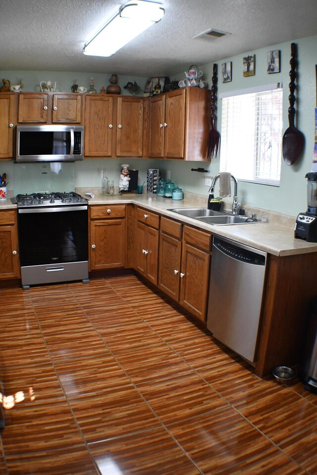 kitchen with a textured ceiling, appliances with stainless steel finishes, dark tile patterned floors, and sink