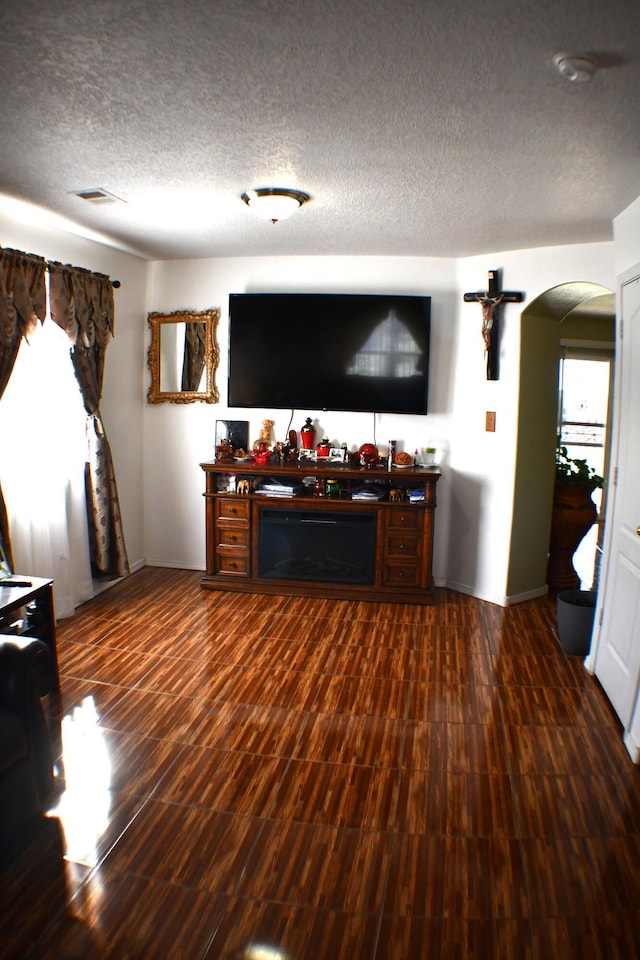 living area featuring arched walkways, dark wood-type flooring, a textured ceiling, and visible vents