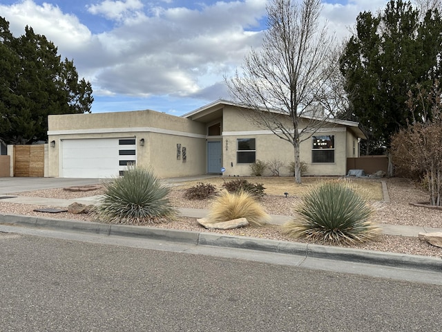 view of front facade featuring stucco siding, a garage, driveway, and fence