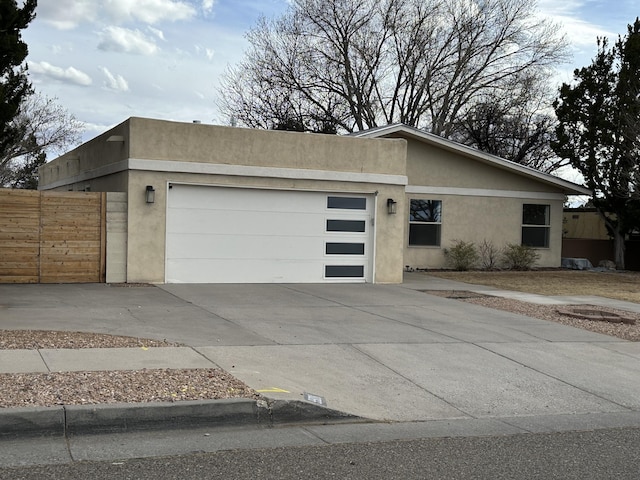 view of front of property featuring fence, a garage, driveway, and stucco siding