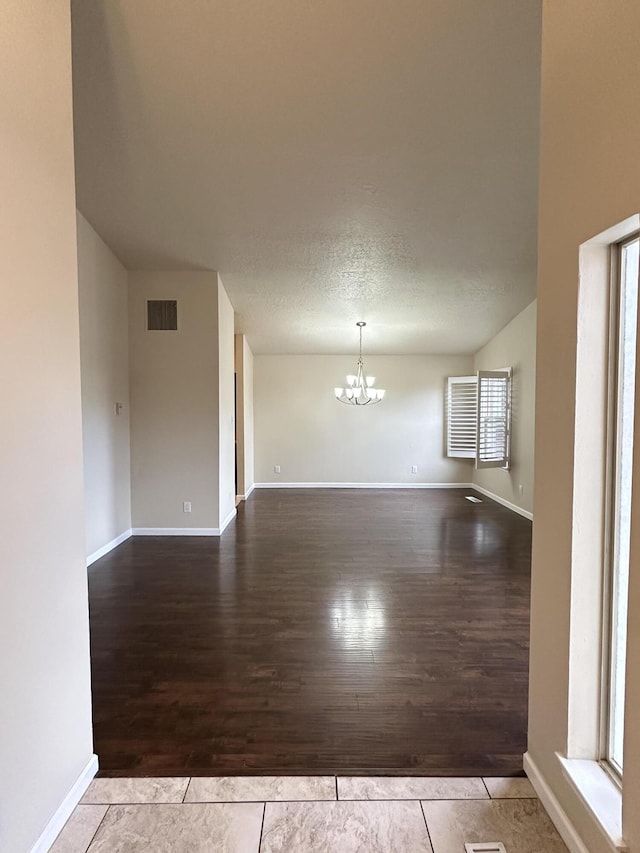 spare room featuring wood finished floors, baseboards, visible vents, a textured ceiling, and a chandelier