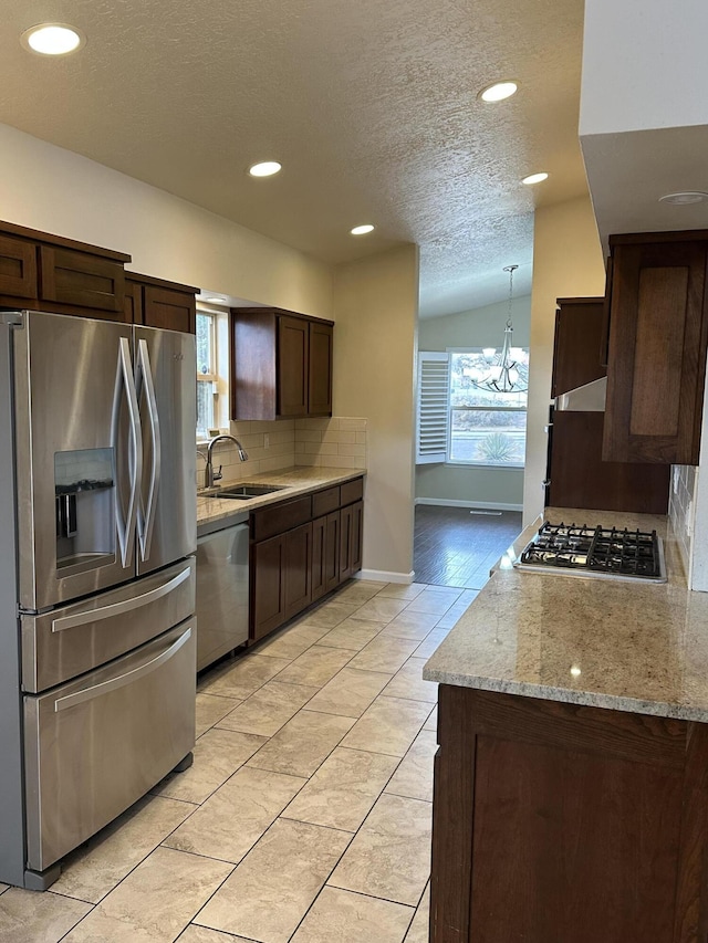 kitchen with backsplash, dark brown cabinets, light stone counters, stainless steel appliances, and a sink