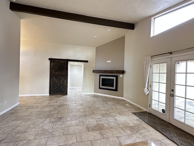 unfurnished living room with a barn door, baseboards, a textured ceiling, and beamed ceiling