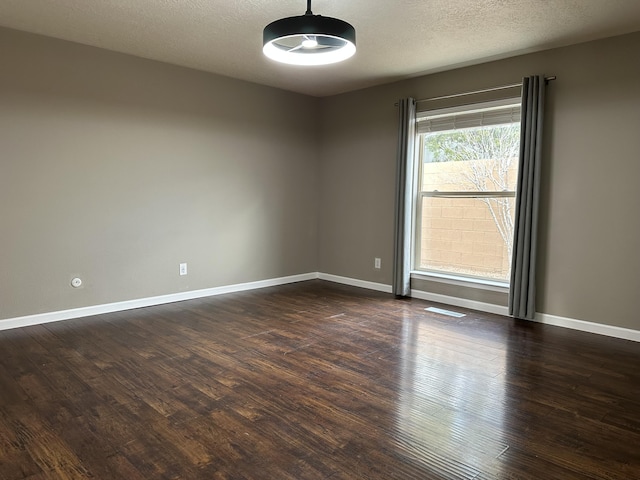 empty room featuring dark wood finished floors, visible vents, a textured ceiling, and baseboards