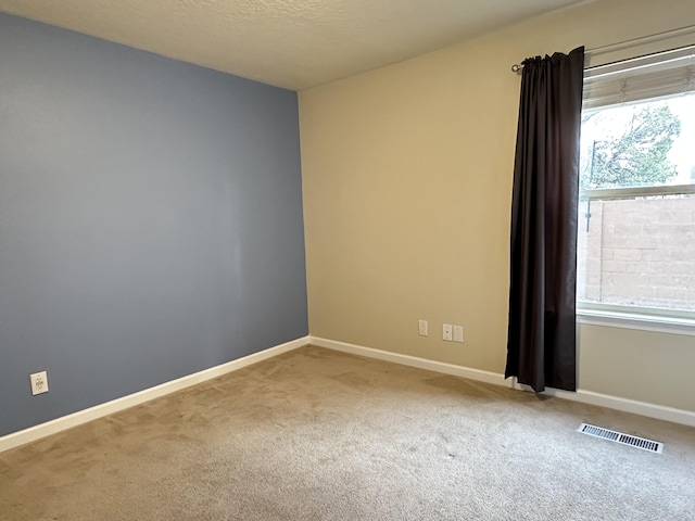 carpeted spare room with a healthy amount of sunlight, visible vents, and baseboards