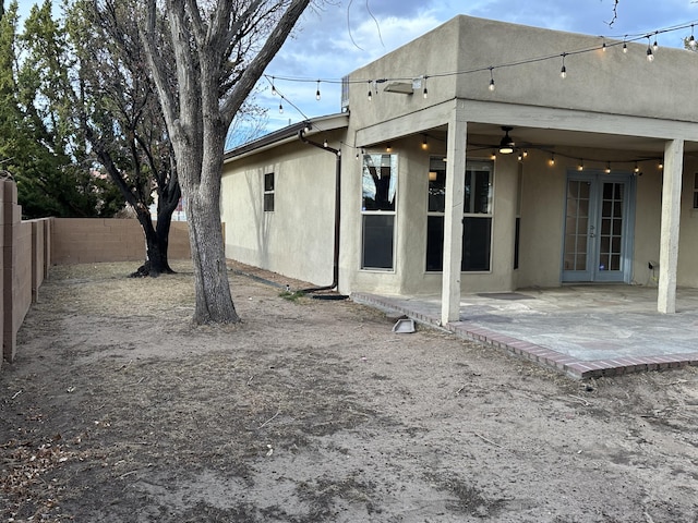 rear view of property with ceiling fan, stucco siding, french doors, a fenced backyard, and a patio area