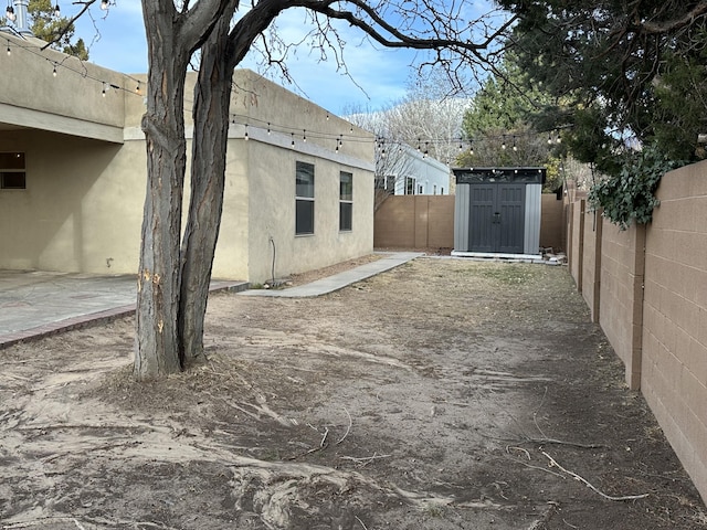 view of yard featuring an outdoor structure, a fenced backyard, a shed, and a patio