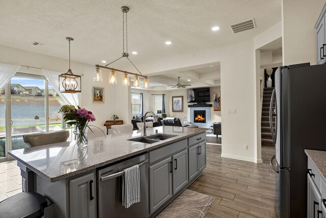 kitchen featuring gray cabinets, sink, light stone countertops, a breakfast bar area, and stainless steel fridge