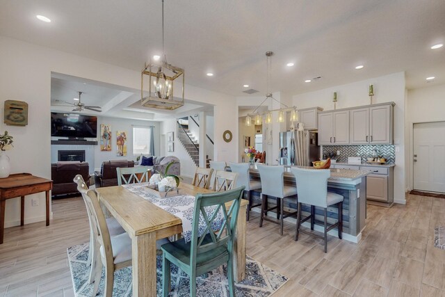 kitchen with decorative light fixtures, wall chimney range hood, a center island with sink, sink, and stainless steel appliances