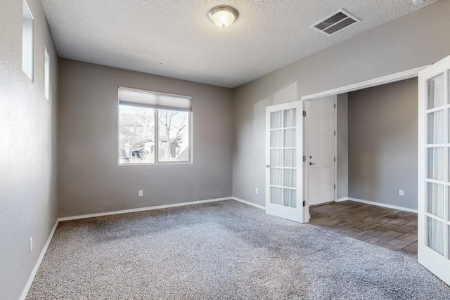 carpeted spare room with a textured ceiling and french doors