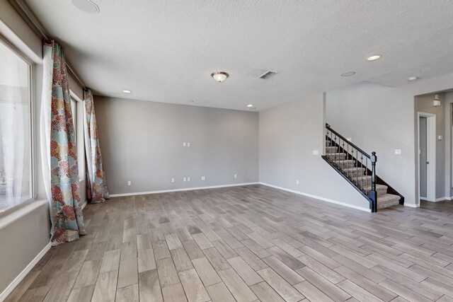 unfurnished room featuring a wealth of natural light, a textured ceiling, and light hardwood / wood-style floors