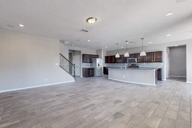 kitchen with stainless steel appliances, a center island with sink, dark brown cabinetry, and decorative light fixtures