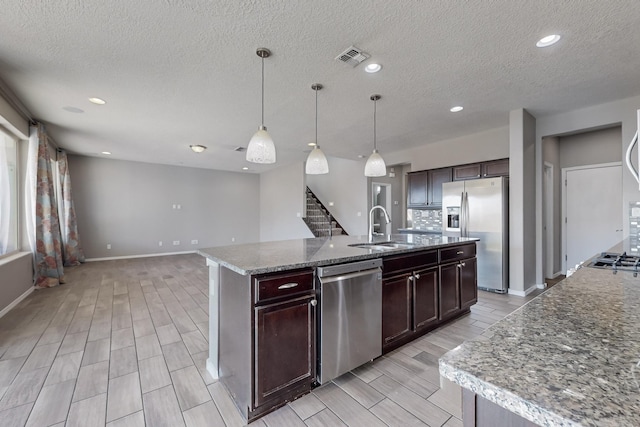 kitchen featuring decorative light fixtures, sink, an island with sink, stainless steel appliances, and dark brown cabinets