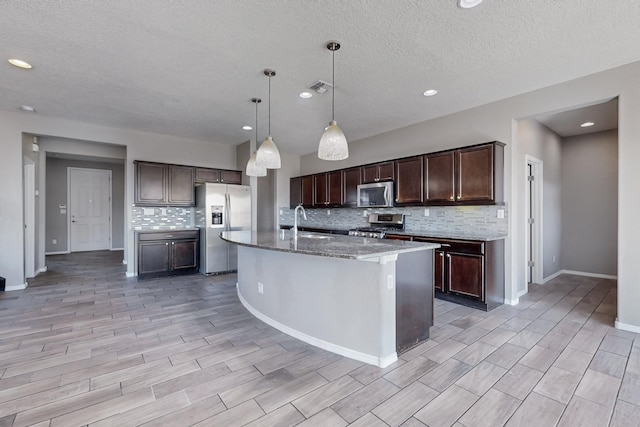 kitchen featuring stainless steel appliances, an island with sink, decorative backsplash, sink, and hanging light fixtures