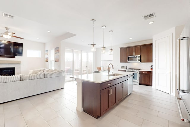 kitchen featuring appliances with stainless steel finishes, pendant lighting, sink, dark brown cabinets, and a center island with sink