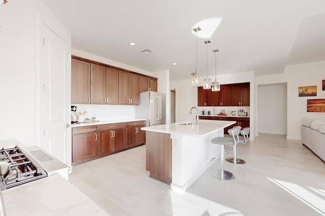 kitchen featuring sink, a kitchen island with sink, a kitchen bar, decorative light fixtures, and high end refrigerator