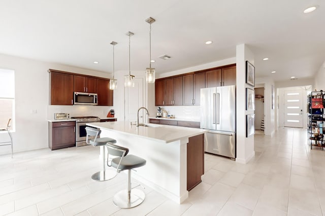 kitchen with sink, a breakfast bar area, hanging light fixtures, stainless steel appliances, and a center island with sink