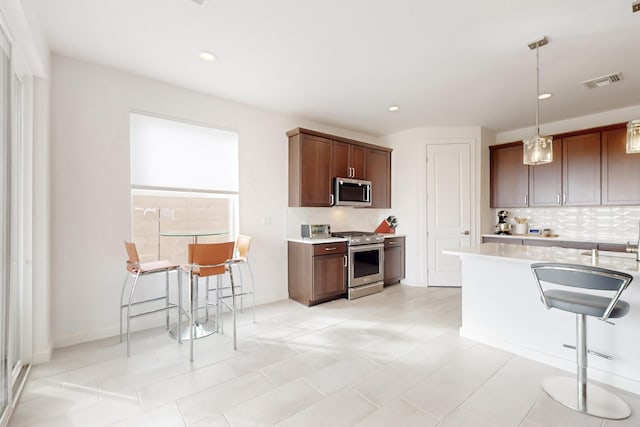 kitchen with light tile patterned flooring, a breakfast bar, pendant lighting, backsplash, and stainless steel appliances