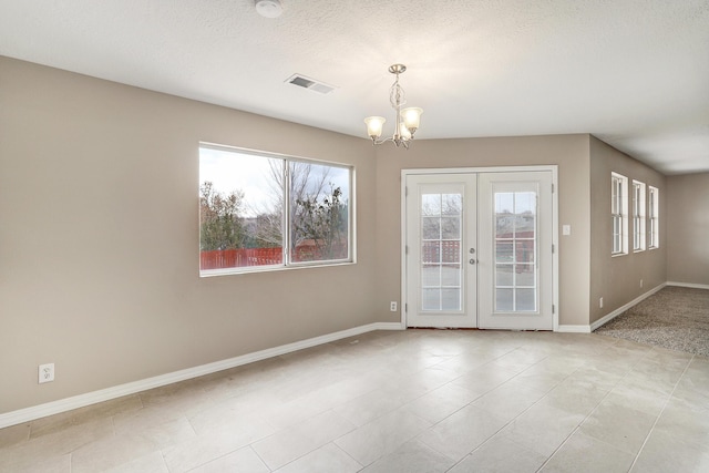 empty room featuring a notable chandelier, a textured ceiling, and french doors