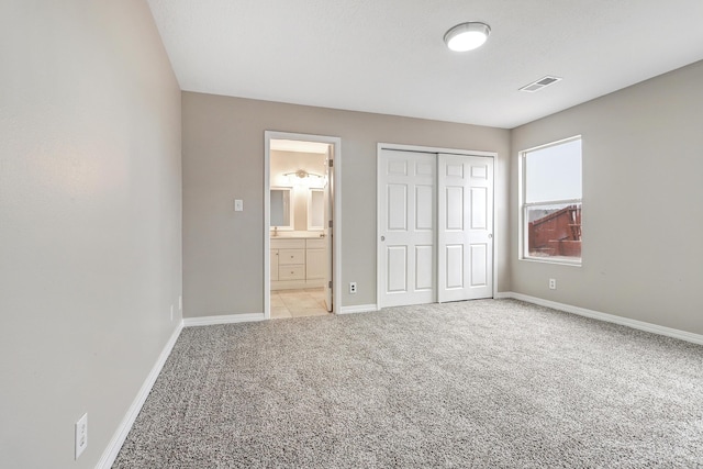 unfurnished bedroom featuring ensuite bathroom, light colored carpet, and a closet