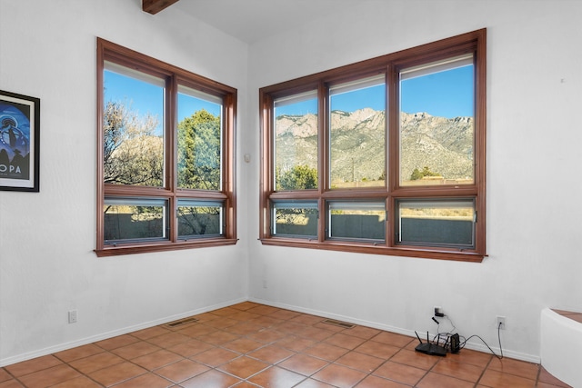 unfurnished room with light tile patterned floors, beam ceiling, and a mountain view