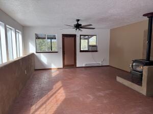 unfurnished living room with ceiling fan, a wood stove, a wealth of natural light, and a baseboard radiator