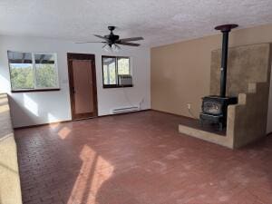 unfurnished living room with a textured ceiling, ceiling fan, and a wood stove