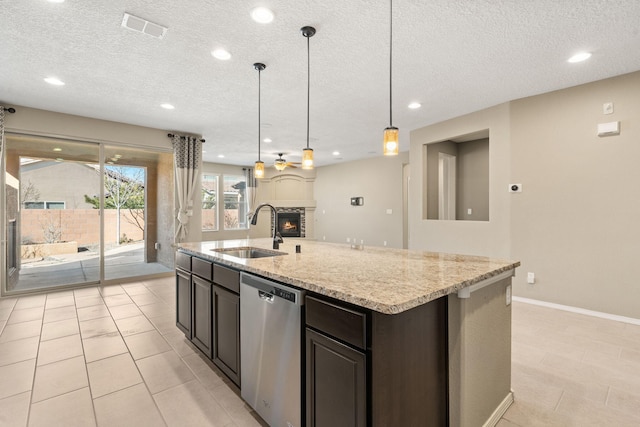 kitchen featuring decorative light fixtures, a fireplace, a center island with sink, stainless steel dishwasher, and sink