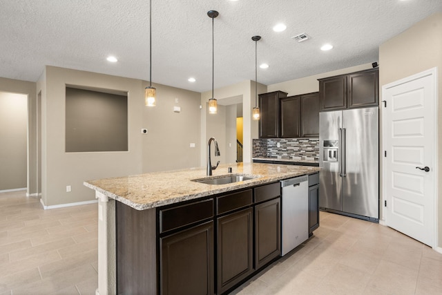 kitchen with an island with sink, appliances with stainless steel finishes, hanging light fixtures, dark brown cabinetry, and sink