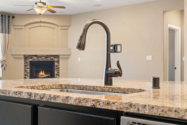 interior details with dishwashing machine, a textured ceiling, sink, ceiling fan, and a tiled fireplace