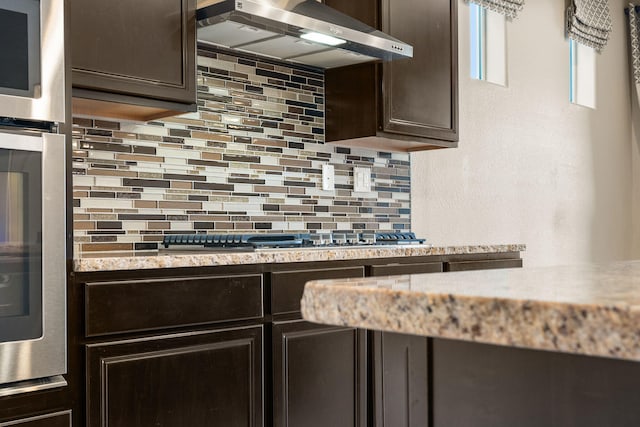 kitchen with dark brown cabinets, stainless steel appliances, extractor fan, and backsplash