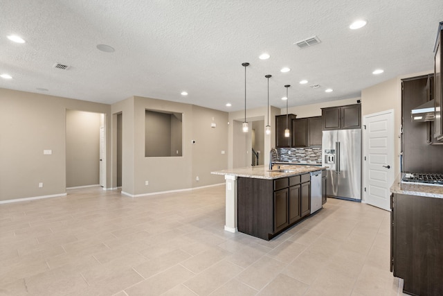 kitchen featuring appliances with stainless steel finishes, tasteful backsplash, a kitchen island with sink, dark brown cabinets, and pendant lighting