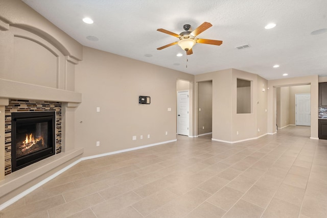 unfurnished living room with ceiling fan, a textured ceiling, light tile patterned floors, and a tile fireplace