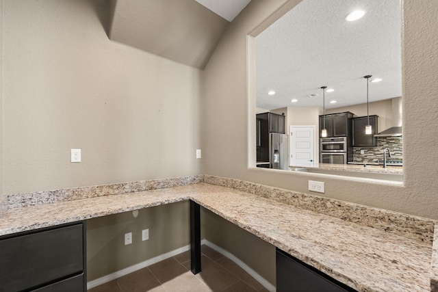 kitchen with stainless steel appliances, wall chimney range hood, tasteful backsplash, light stone countertops, and sink