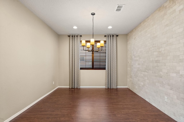 unfurnished dining area featuring dark hardwood / wood-style flooring, brick wall, an inviting chandelier, and a textured ceiling