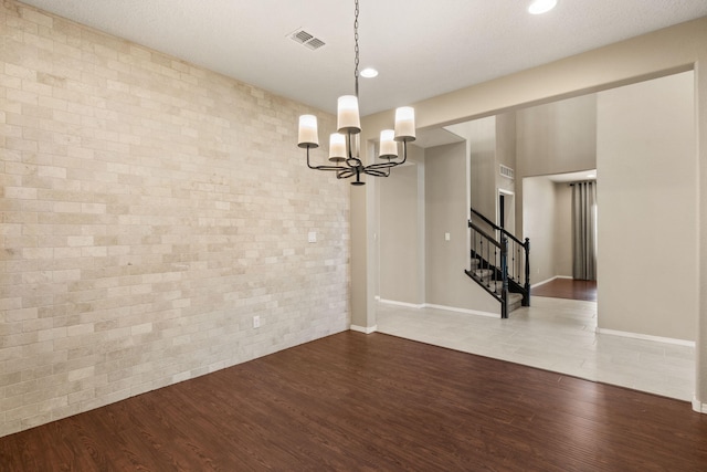 unfurnished dining area with wood-type flooring, a notable chandelier, and brick wall