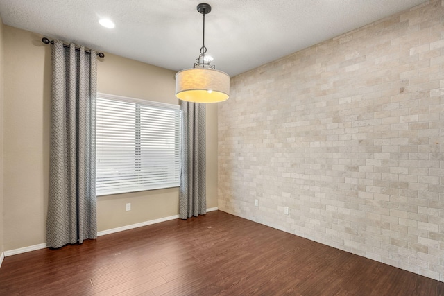 spare room featuring dark wood-type flooring, brick wall, and a textured ceiling