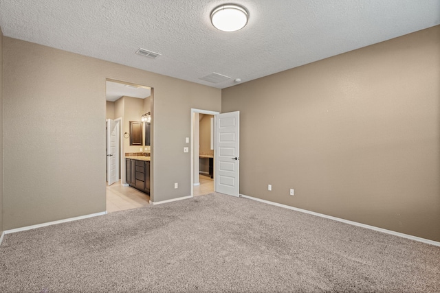 unfurnished bedroom featuring a textured ceiling, ensuite bathroom, and light colored carpet