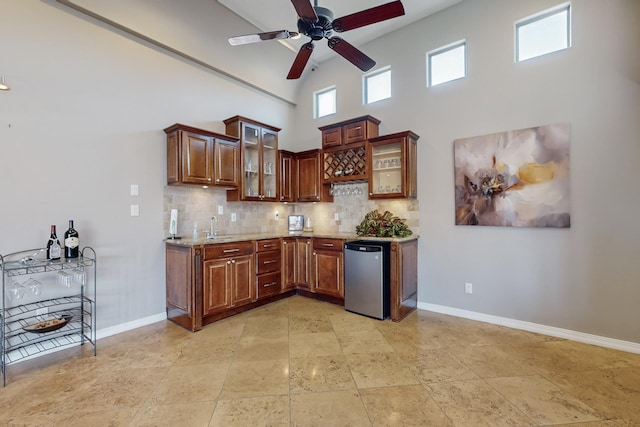 kitchen with ceiling fan, decorative backsplash, fridge, a towering ceiling, and light stone counters