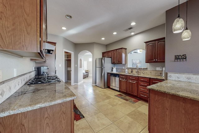 kitchen with light stone countertops, exhaust hood, decorative light fixtures, stainless steel appliances, and sink